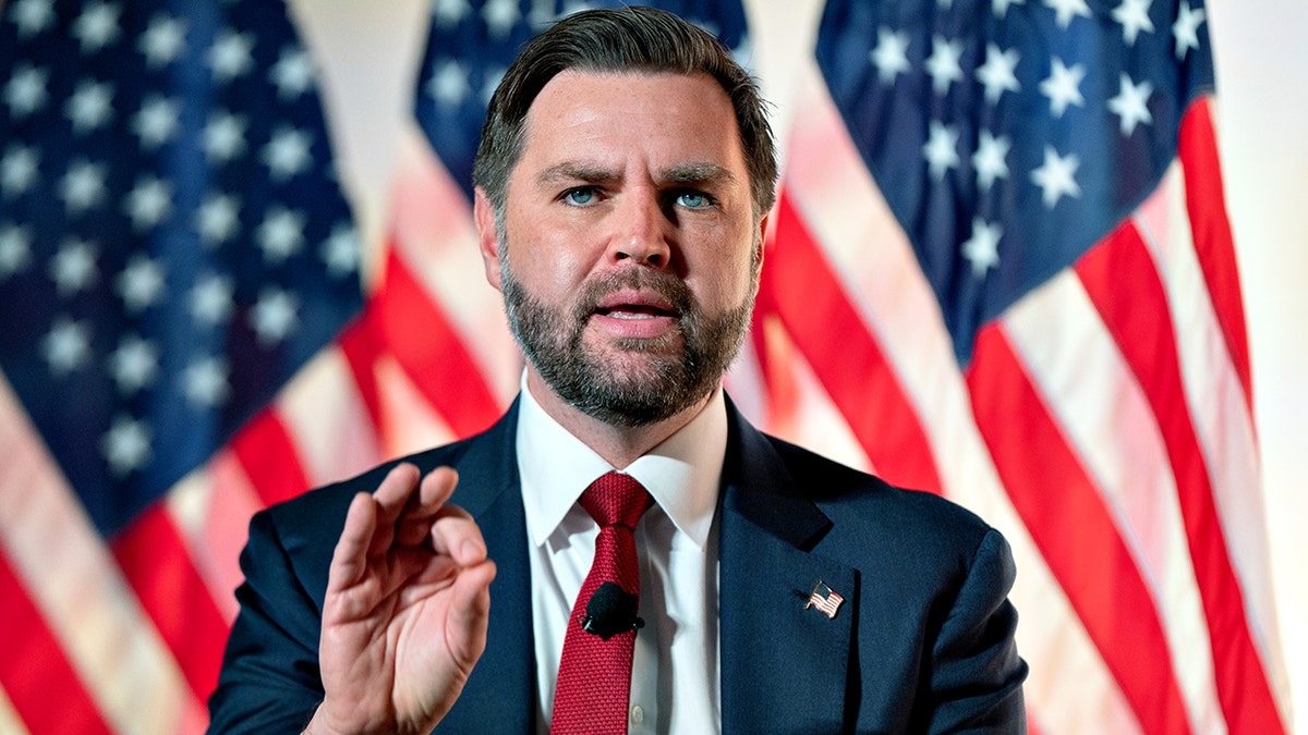 Vice President JD Vance gestures while speaking in front of American flags