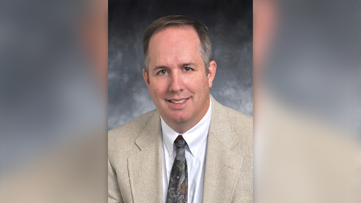 Andrew Wimsatt in a tan suit jacket, white shirt and paisley tie