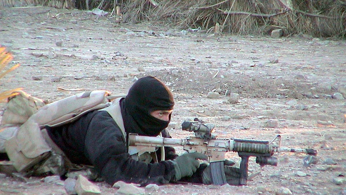 U.S. Navy Seal member providing cover for teammates in a desert environment
