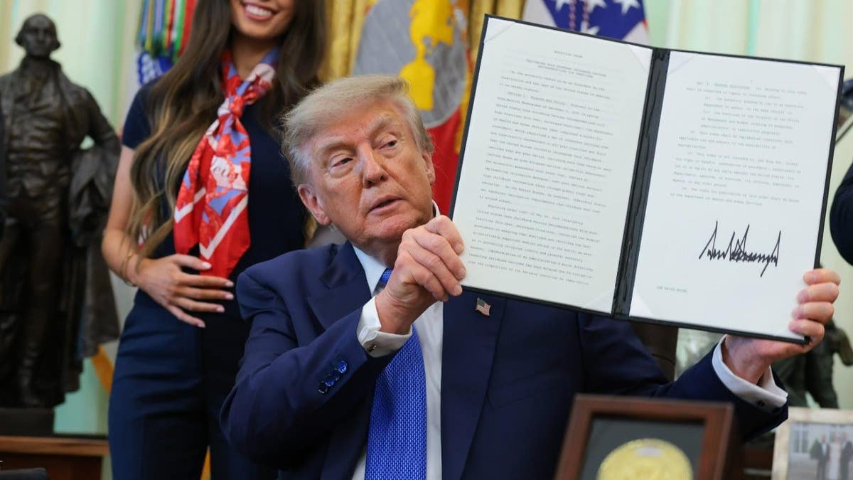 President Donald Trump holds up a signed executive order